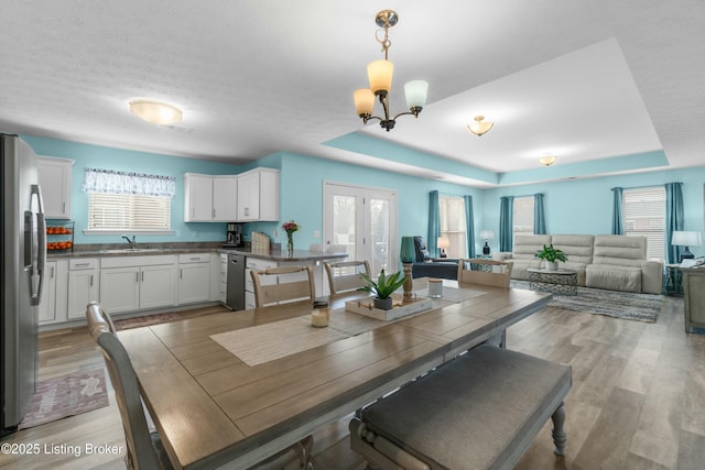 dining space with a chandelier, a textured ceiling, a raised ceiling, and light wood-style flooring