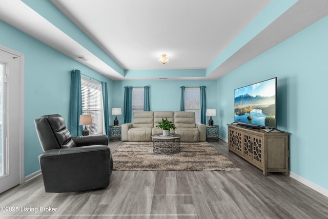 living area with baseboards, visible vents, a tray ceiling, and wood finished floors