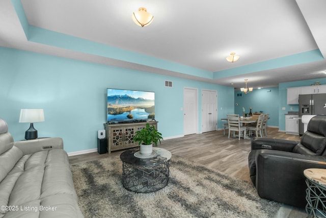 living area featuring a tray ceiling, visible vents, baseboards, and wood finished floors