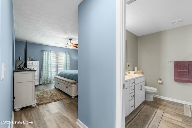 bathroom featuring visible vents, baseboards, toilet, wood finished floors, and vanity