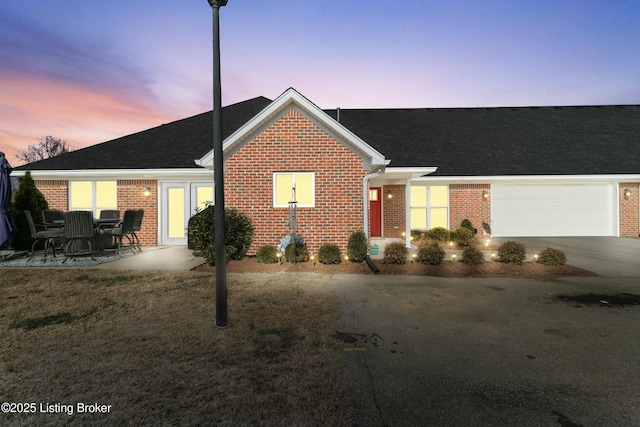 ranch-style home featuring a garage, concrete driveway, brick siding, and roof with shingles