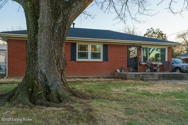 ranch-style house featuring brick siding, a front yard, and a shingled roof