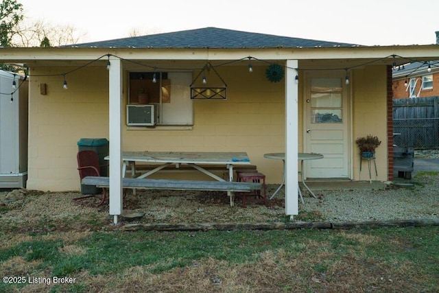 exterior space with cooling unit, concrete block siding, a shingled roof, and fence