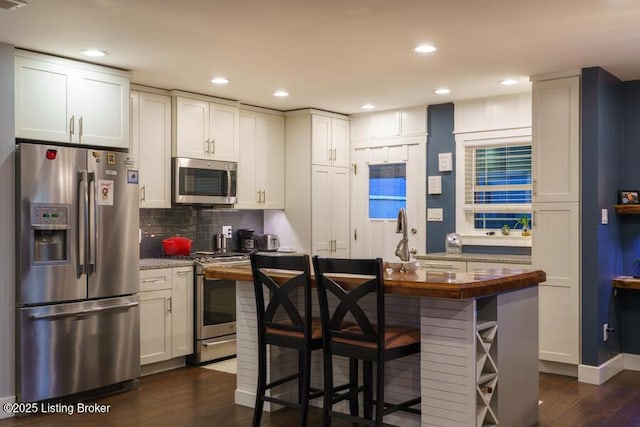 kitchen featuring decorative backsplash, a kitchen breakfast bar, dark wood-style floors, white cabinets, and stainless steel appliances