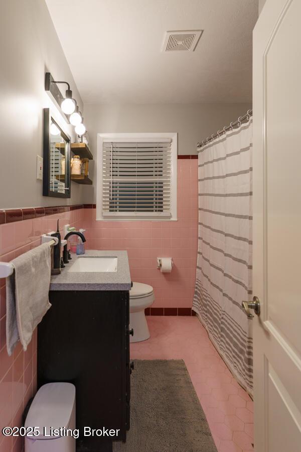 bathroom with visible vents, tile walls, a wainscoted wall, toilet, and vanity