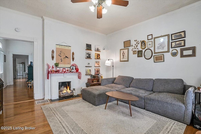 living area featuring a ceiling fan, wood finished floors, a lit fireplace, a textured ceiling, and crown molding