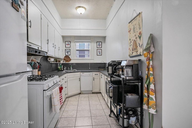 kitchen with light tile patterned floors, under cabinet range hood, white appliances, white cabinets, and dark countertops