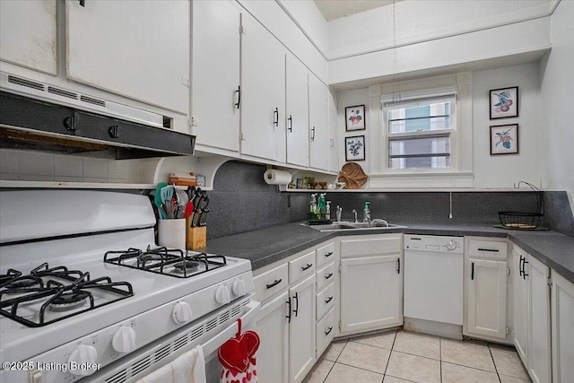 kitchen with light tile patterned floors, white appliances, a sink, white cabinetry, and dark countertops