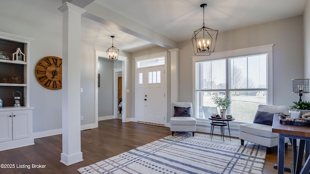 entrance foyer featuring dark wood-style flooring, baseboards, a notable chandelier, and ornate columns