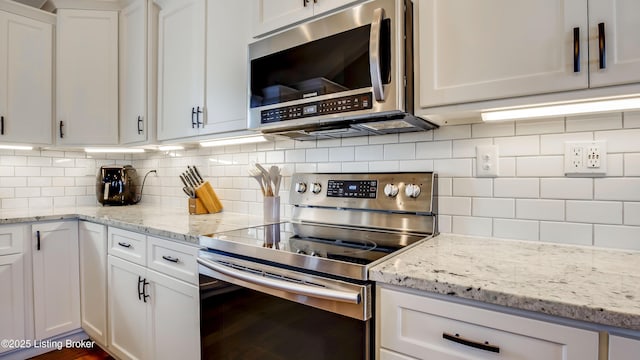 kitchen with stainless steel appliances, white cabinetry, backsplash, and light stone counters