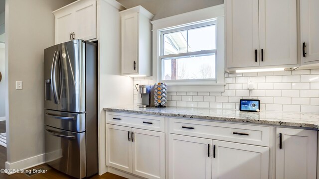 kitchen featuring light stone counters, stainless steel fridge with ice dispenser, backsplash, white cabinetry, and baseboards