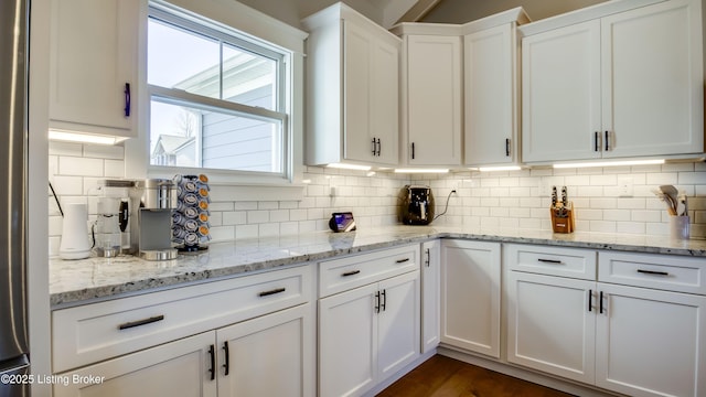 kitchen with light stone counters, white cabinetry, and backsplash