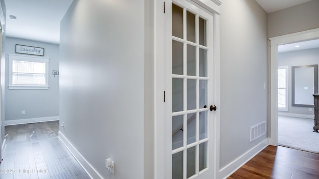 hall with baseboards, visible vents, a wealth of natural light, and wood finished floors