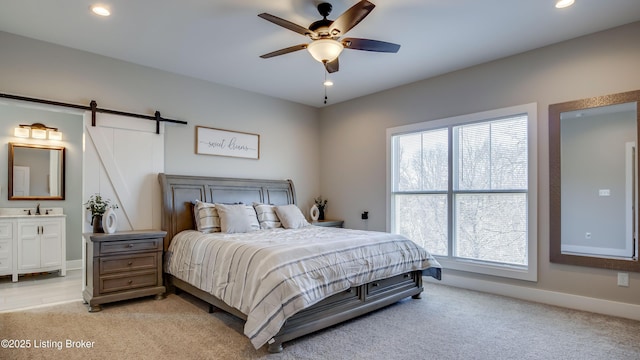 bedroom with a barn door, recessed lighting, light carpet, baseboards, and ensuite bath