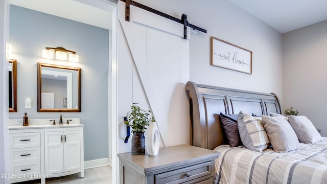 bedroom featuring baseboards, a sink, light wood finished floors, and a barn door