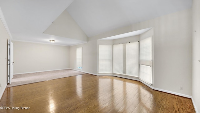 empty room featuring lofted ceiling, crown molding, hardwood / wood-style flooring, and baseboards