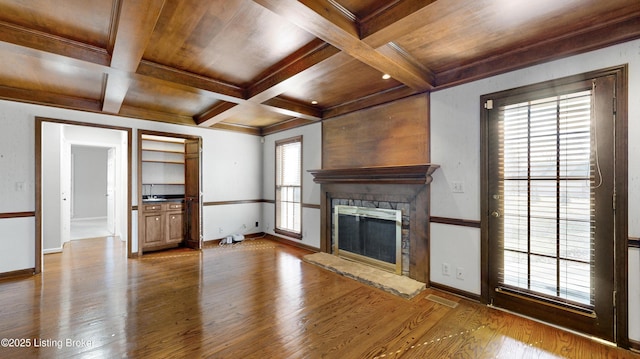 unfurnished living room with baseboards, coffered ceiling, wood finished floors, and a stone fireplace