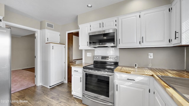 kitchen with appliances with stainless steel finishes, wood finished floors, light countertops, and white cabinetry