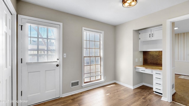 doorway featuring built in study area, visible vents, baseboards, and wood finished floors