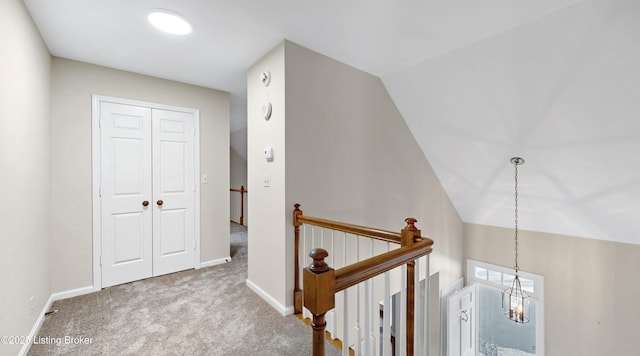 hallway featuring carpet floors, baseboards, vaulted ceiling, and an upstairs landing