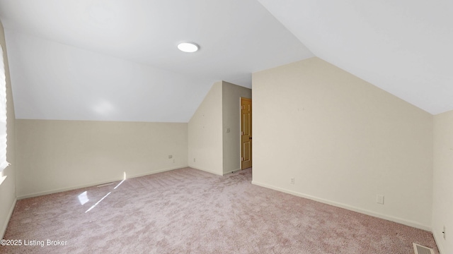 additional living space featuring baseboards, visible vents, vaulted ceiling, and light colored carpet