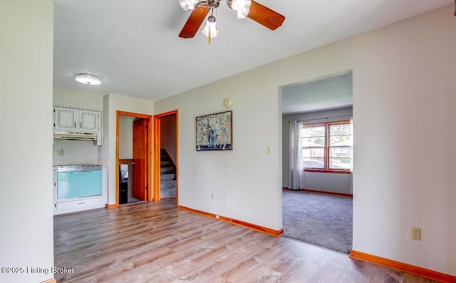 empty room with a ceiling fan, baseboards, stairway, and light wood finished floors