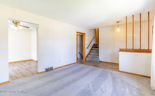 spare room with carpet flooring, a ceiling fan, visible vents, stairs, and baseboards