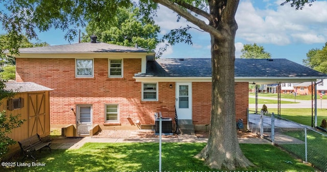 back of house featuring roof with shingles, brick siding, a lawn, fence, and cooling unit