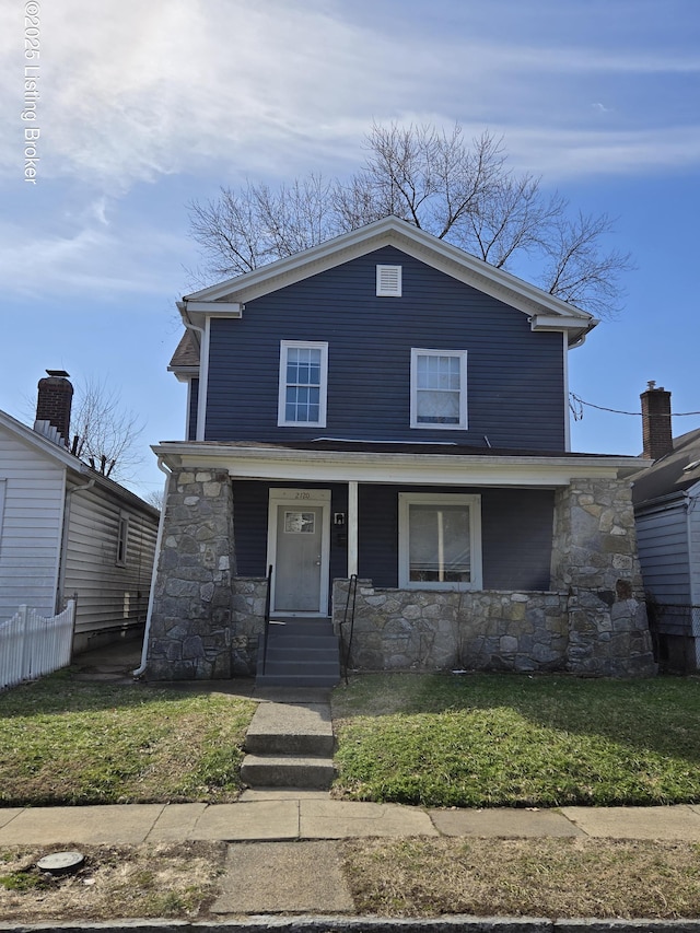 view of front of house featuring covered porch, stone siding, a front lawn, and fence