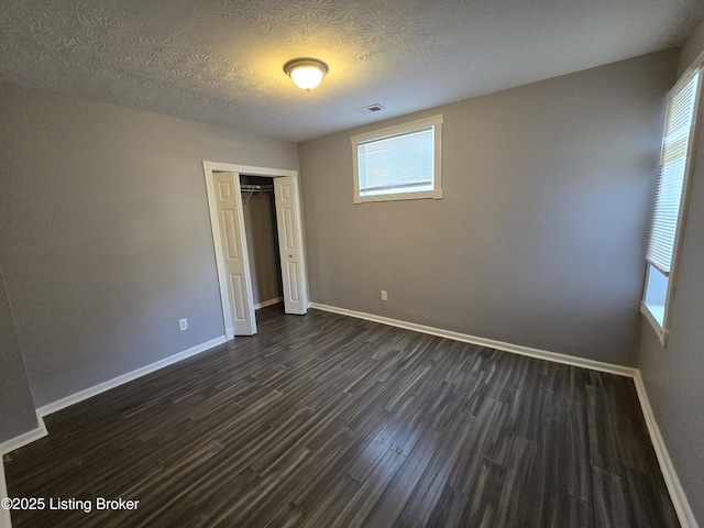 unfurnished bedroom with a textured ceiling, dark wood-style flooring, visible vents, baseboards, and a closet