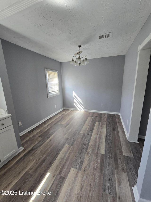 unfurnished dining area featuring a textured ceiling, dark wood-style flooring, visible vents, and an inviting chandelier