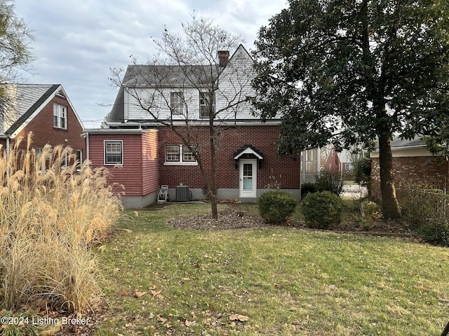 view of front of home with a chimney, central AC unit, a front lawn, and brick siding