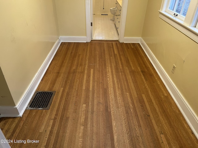 hallway with baseboards, visible vents, and wood finished floors