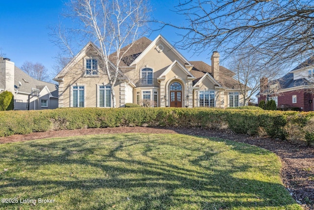 view of front of house featuring a chimney, a front lawn, and stucco siding