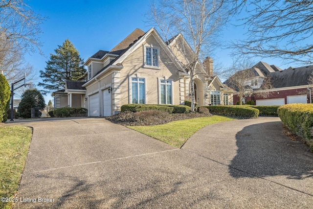 traditional-style home with an attached garage, a chimney, concrete driveway, and stucco siding