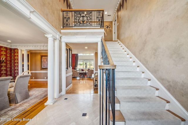 staircase with a towering ceiling, ornate columns, baseboards, and ornamental molding