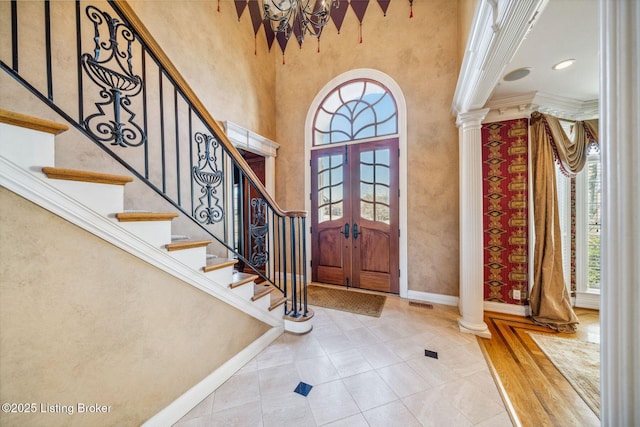 foyer entrance with a high ceiling, baseboards, french doors, ornate columns, and crown molding