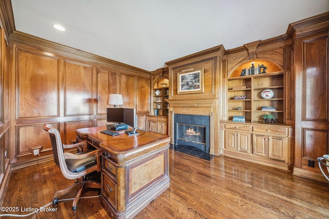 home office featuring built in shelves, a high end fireplace, and dark wood finished floors