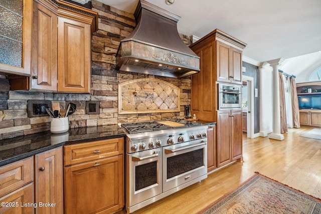 kitchen featuring decorative columns, custom range hood, stainless steel appliances, light wood-style floors, and backsplash