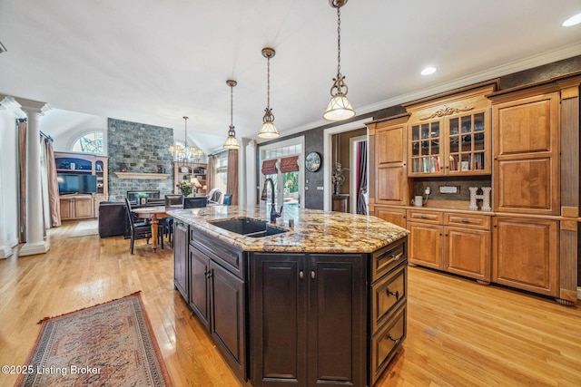 kitchen with lofted ceiling, ornamental molding, light wood-style floors, a sink, and ornate columns