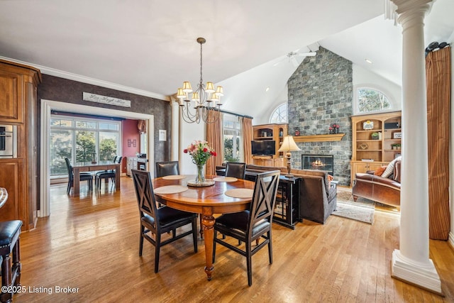 dining room featuring a stone fireplace, a wealth of natural light, light wood-style flooring, and ornate columns