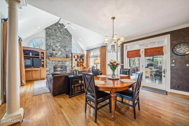 dining space featuring high vaulted ceiling, a stone fireplace, light wood-type flooring, and ornate columns