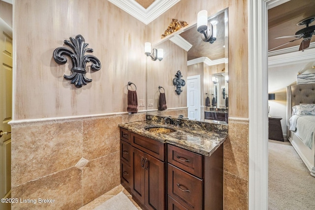 ensuite bathroom featuring ceiling fan, connected bathroom, tile walls, vanity, and crown molding