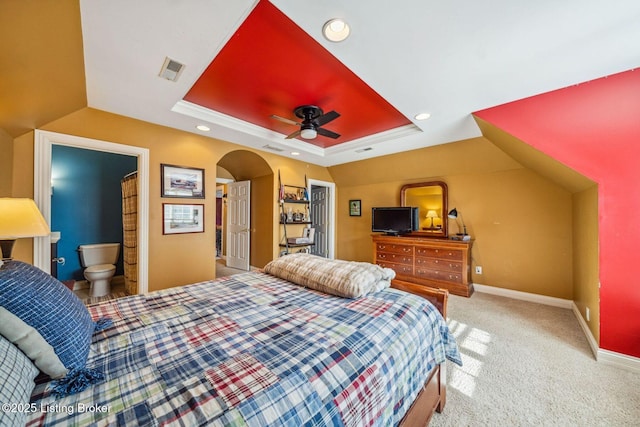 bedroom featuring carpet floors, arched walkways, a raised ceiling, visible vents, and baseboards