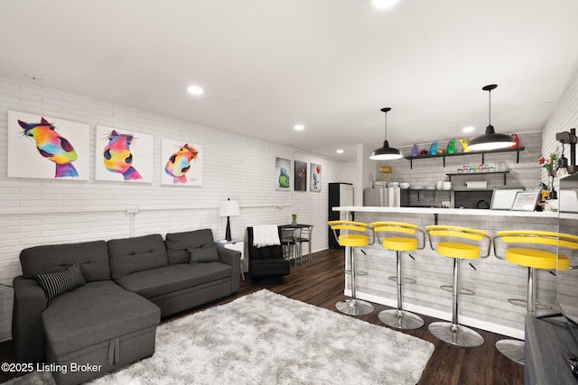 living area featuring recessed lighting, indoor wet bar, brick wall, and wood finished floors