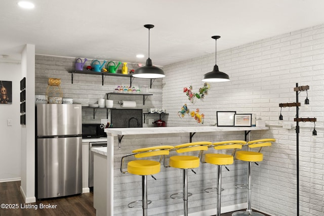 kitchen featuring black microwave, brick wall, freestanding refrigerator, dark wood-style floors, and pendant lighting