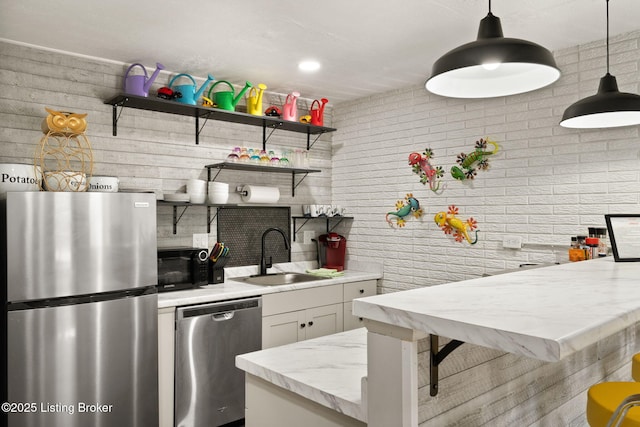 kitchen with pendant lighting, open shelves, appliances with stainless steel finishes, a sink, and light stone countertops