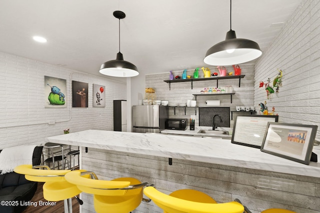 kitchen featuring brick wall, light stone counters, a sink, and freestanding refrigerator