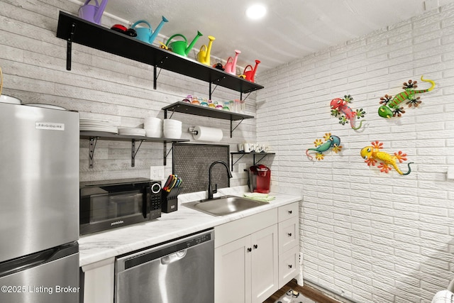 kitchen featuring open shelves, appliances with stainless steel finishes, white cabinetry, a sink, and brick wall