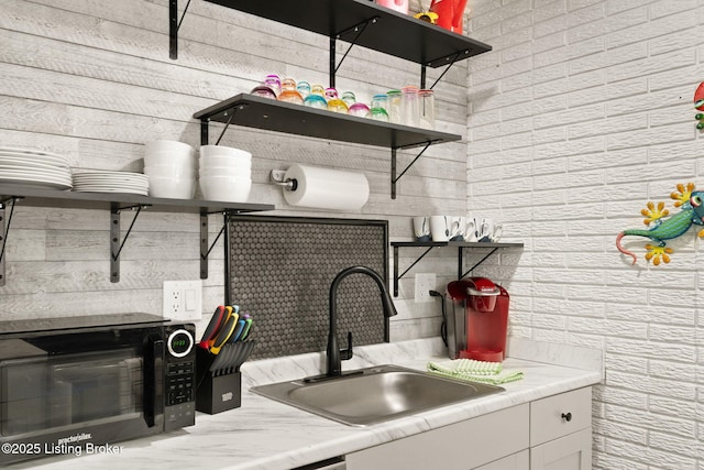 kitchen with black microwave, a sink, white cabinetry, open shelves, and tasteful backsplash